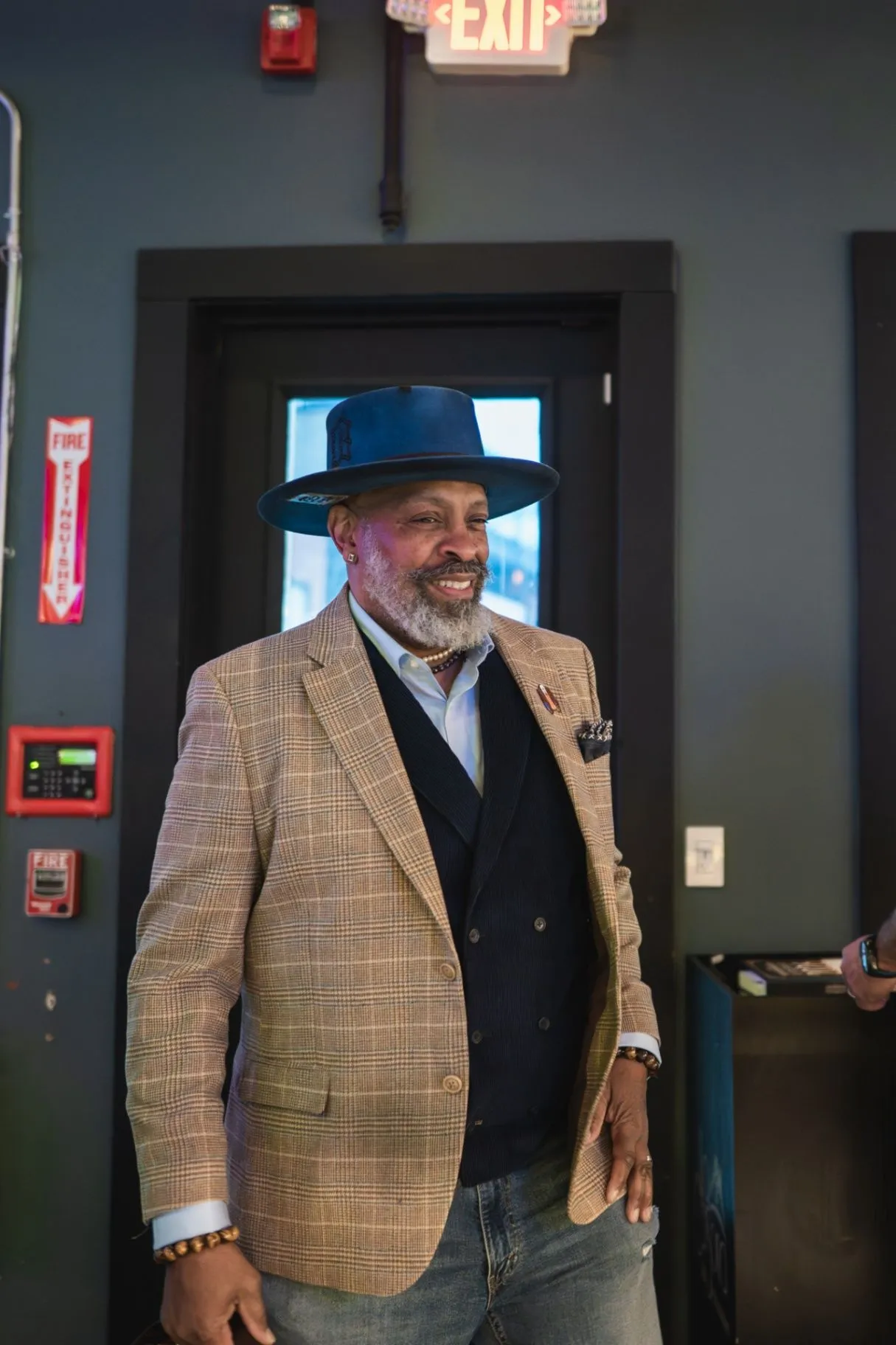 A Society guest in a patterned blazer and hat smiling inside the lounge