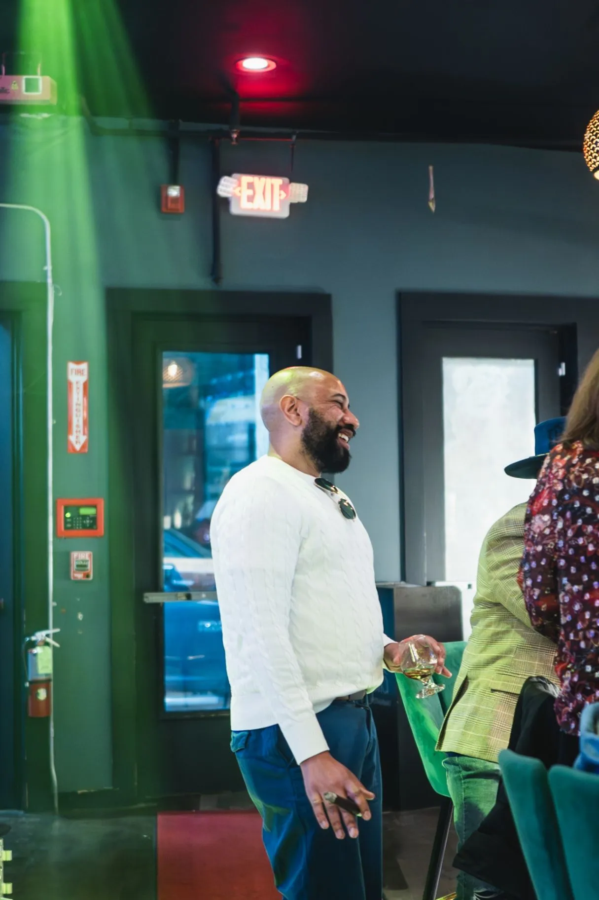 A Society guest smiling with a drink while friends gather under green and red lights