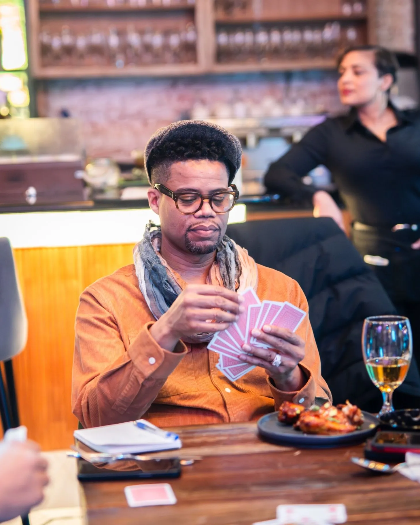 A Society guest holding playing cards at a table with drinks and shared food